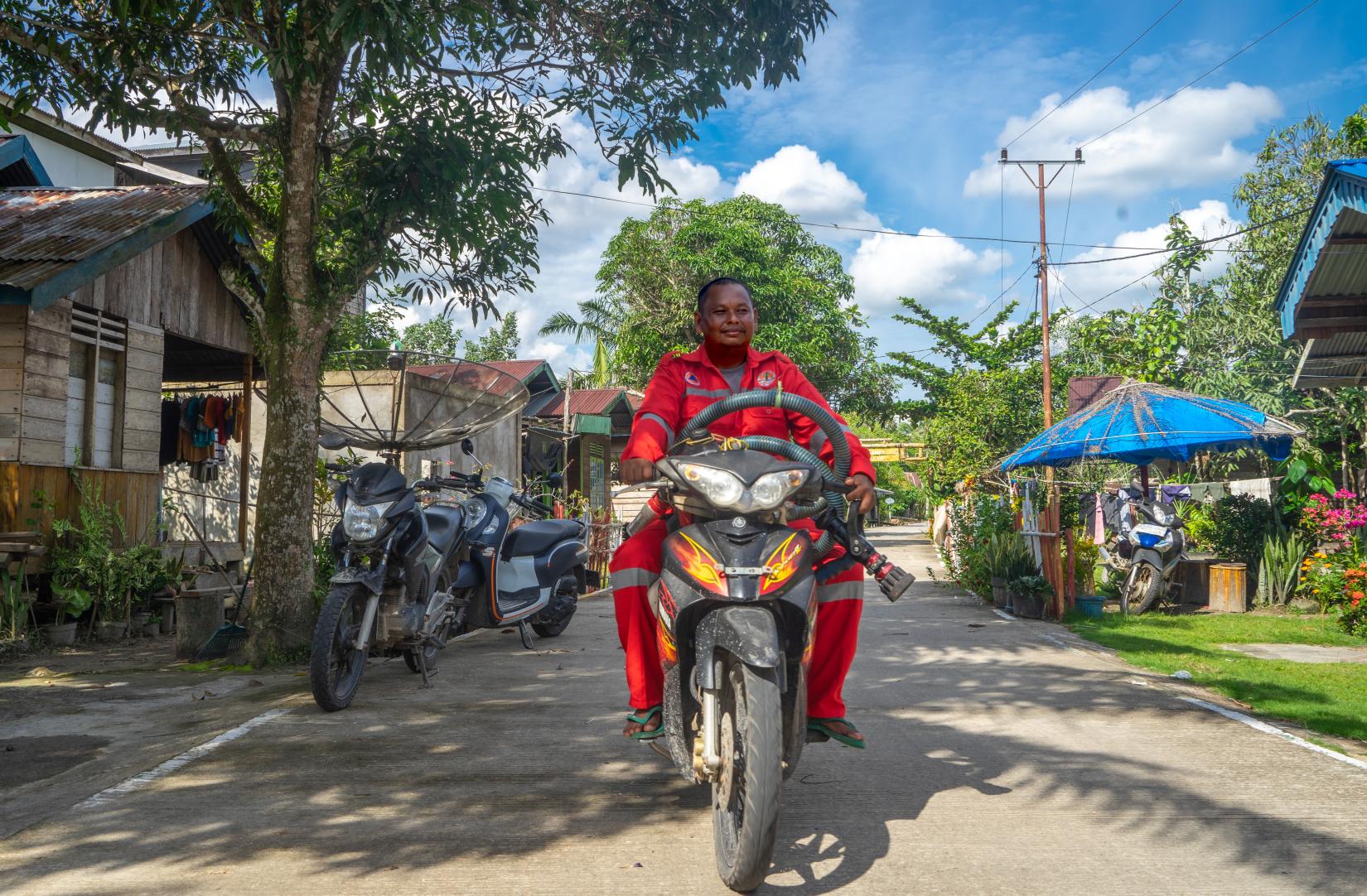 A man in fire fighter suit is riding a motorcycle in a village