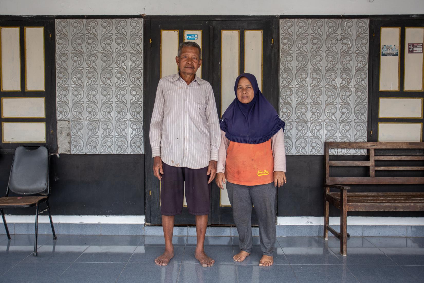 An elderly man and woman standing in front of their house