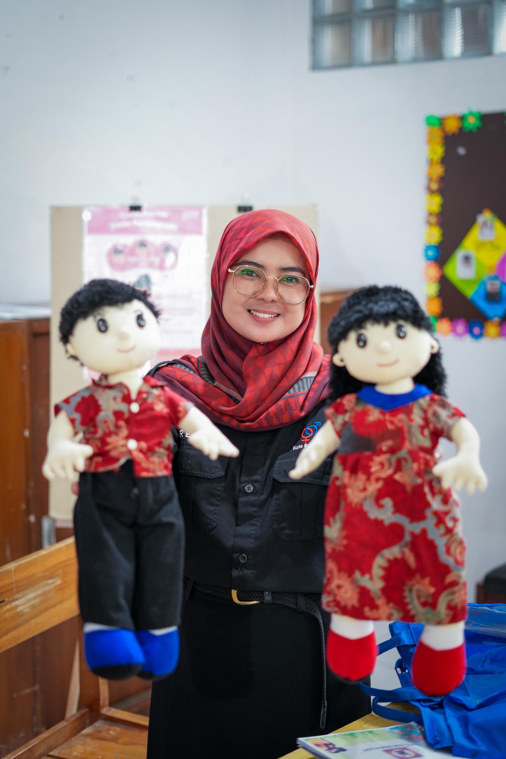 Rina Gusnaeni holding two dolls of a girl and a boy