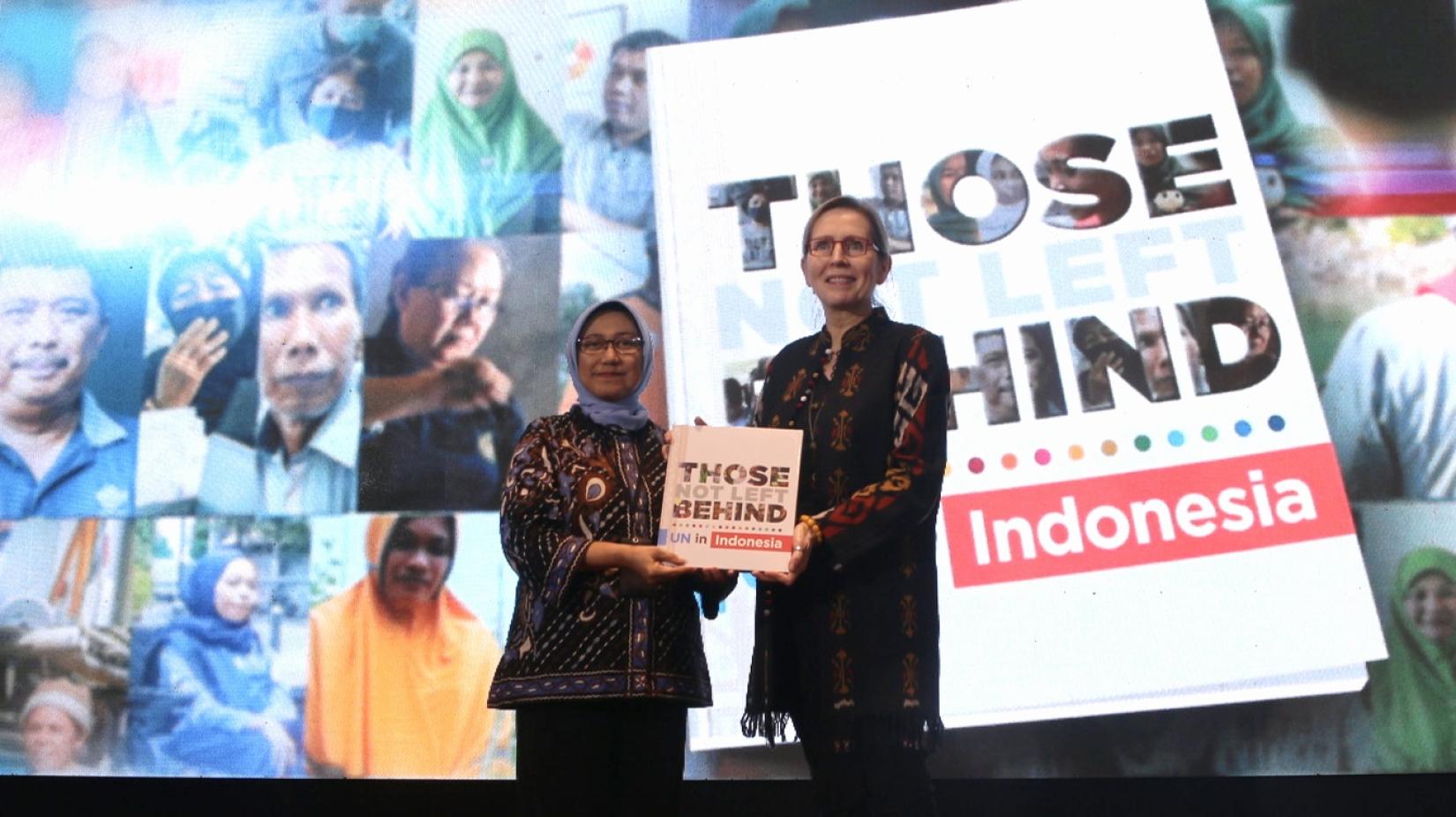 Valerie Julliand and Vivi Yulaswati is posing with Those Not Left Behind book on a stage