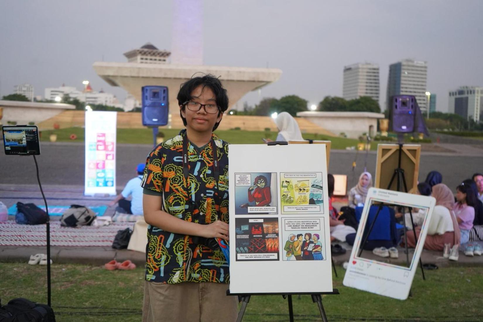 One of the winners of comic competition poses with his winning comic strip in front of Monas