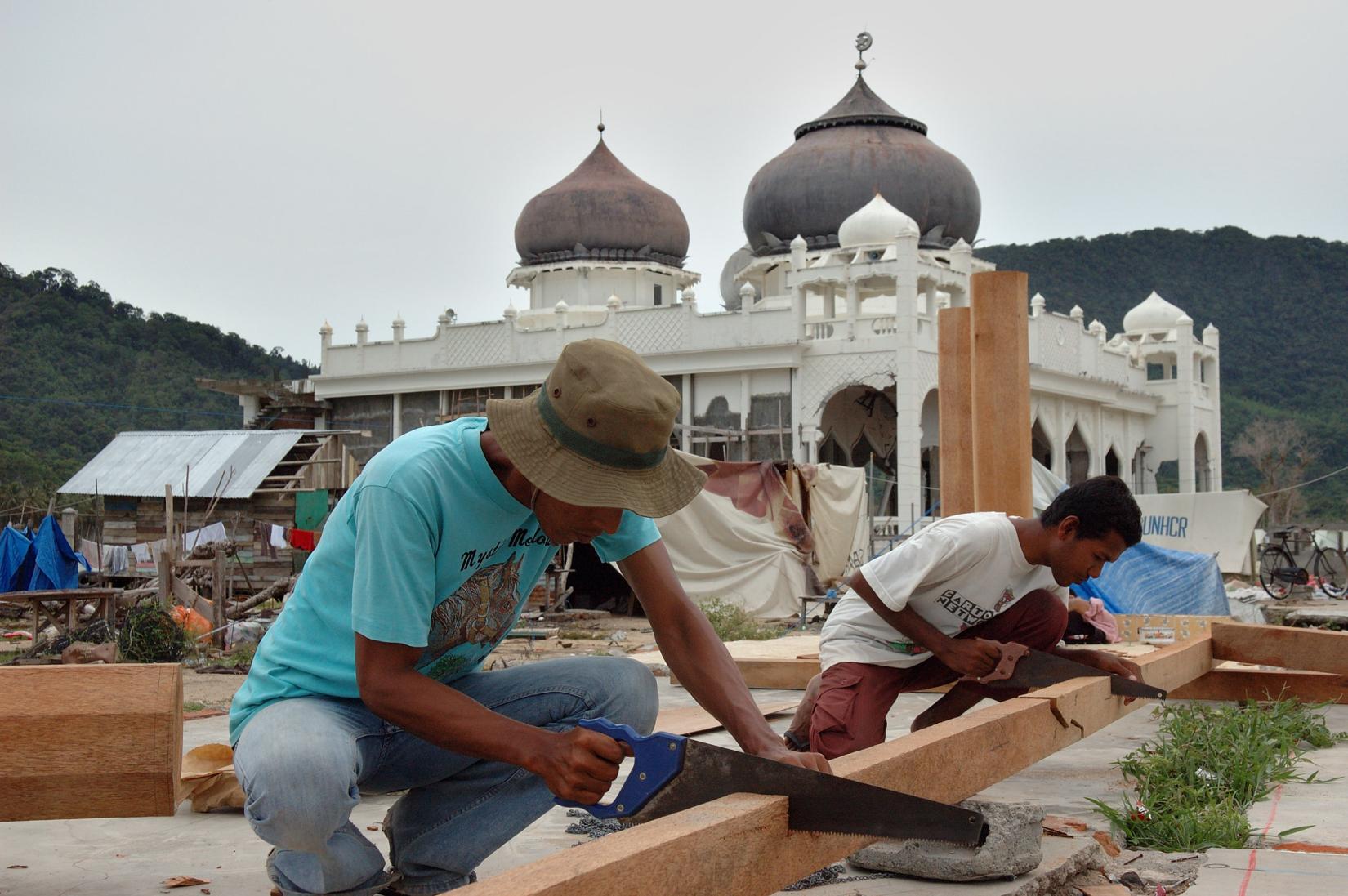 The reconstruction work in Aceh Province and Nias Island lasted several years. Nonetheless, in six months, the local people has exhibited incredible resilience and is boldly returning to their life. In this photograph, a man is actively working to reconstruct a home in a tsunami-devastated district of Banda Aceh.