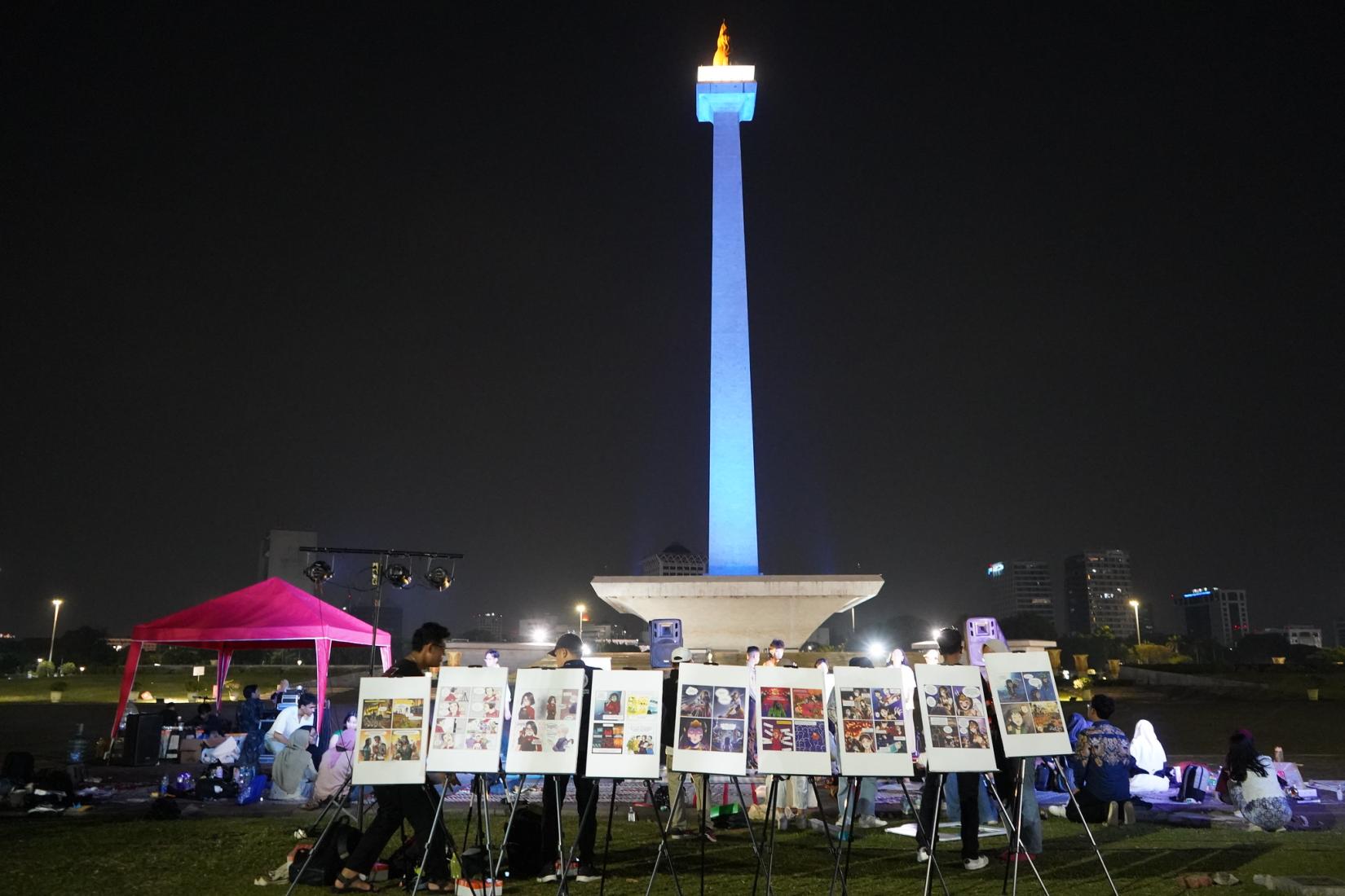 Nine panels of comics displayed in front of blue-lit Monas