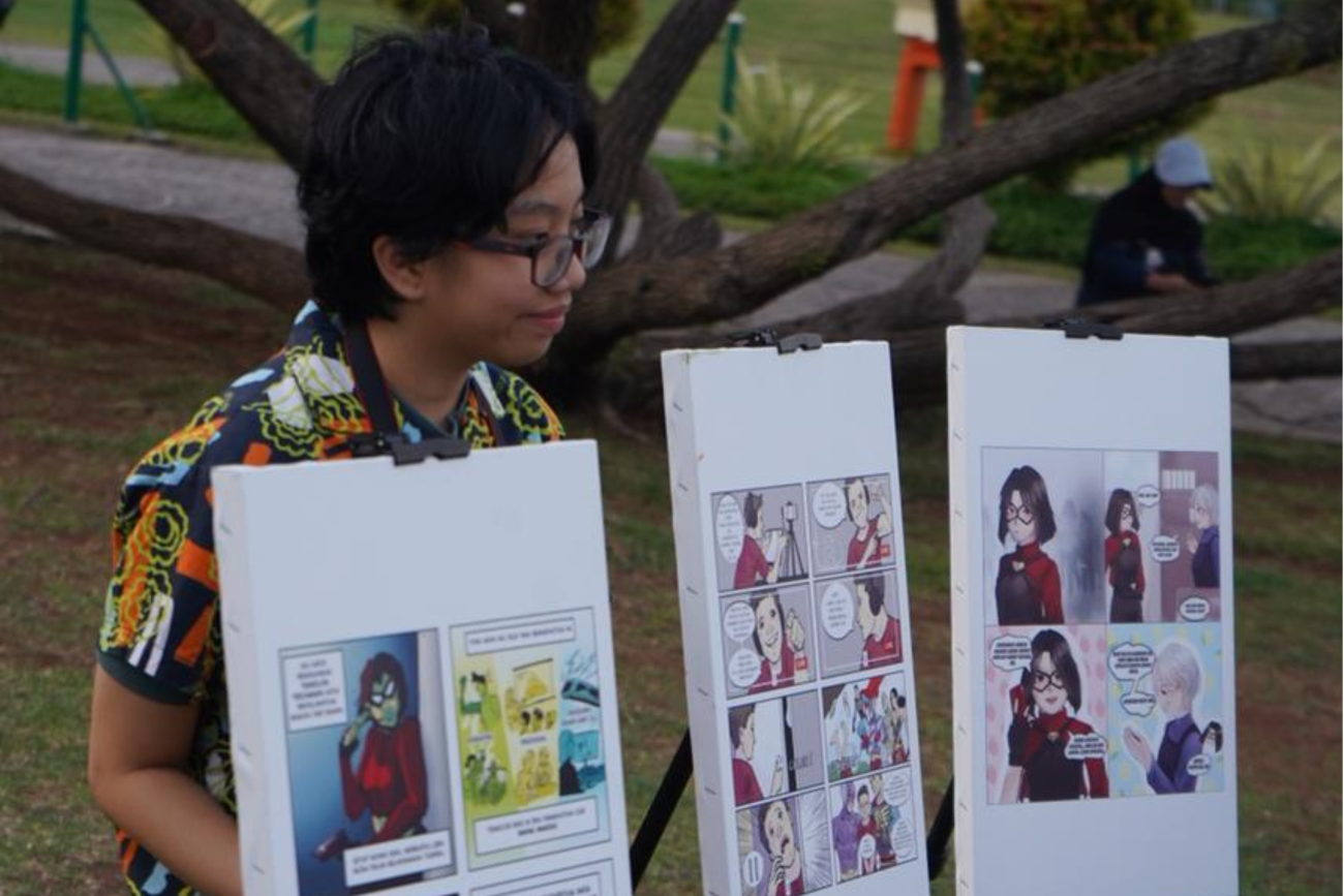 One of the winners of comic competition poses with her winning comic strip in front of Monas