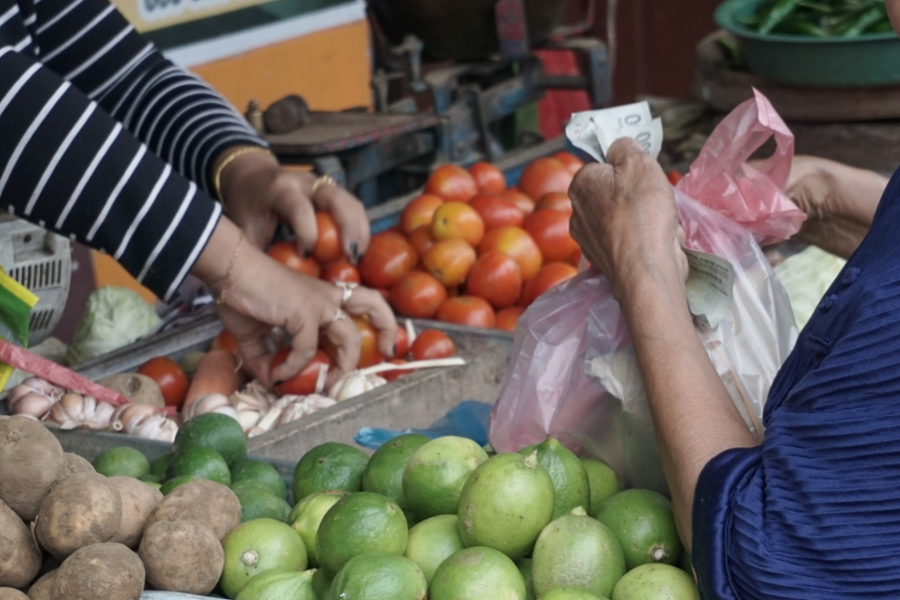 Seorang penduduk setempat berbelanja tomat di toko sayur. Mereka memegang sejumlah uang sambil menunggu pesanan mereka.