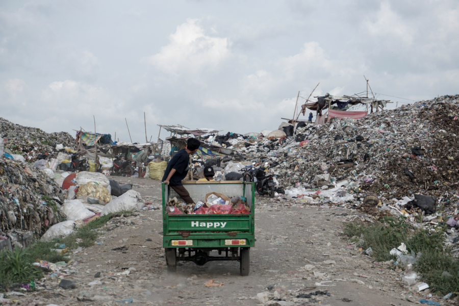 Tempat pembuangan sampah dipenuhi dengan berbagai sampah yang tidak dipisahkan. Di tengah adalah seorang pria yang mengendarai truk pengangkut sampah.