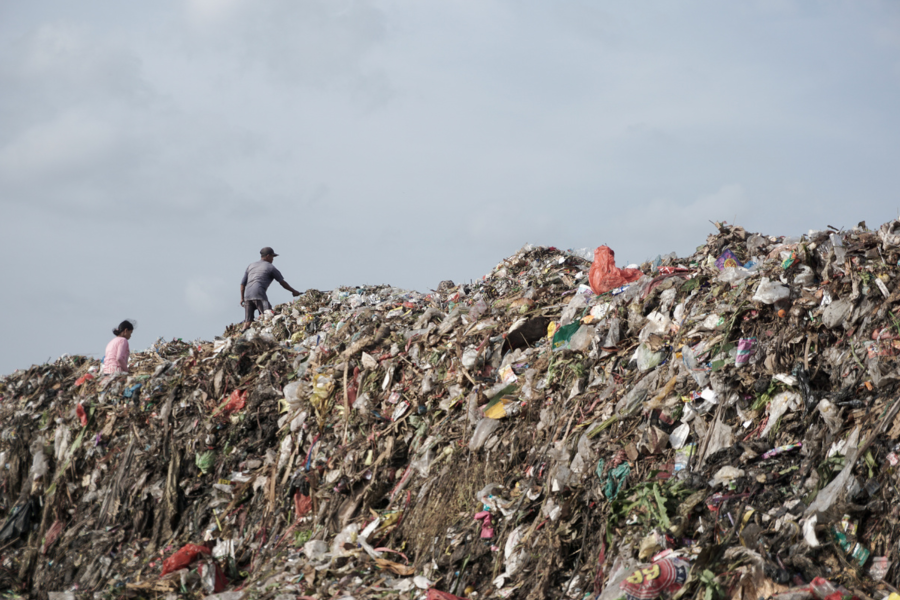 Bukit sampah yang menjulang tinggi di lokasi TPA dipenuhi berbagai sampah yang tak terpisahkan. Seorang pria dan seorang wanita mendaki gunung sampah.