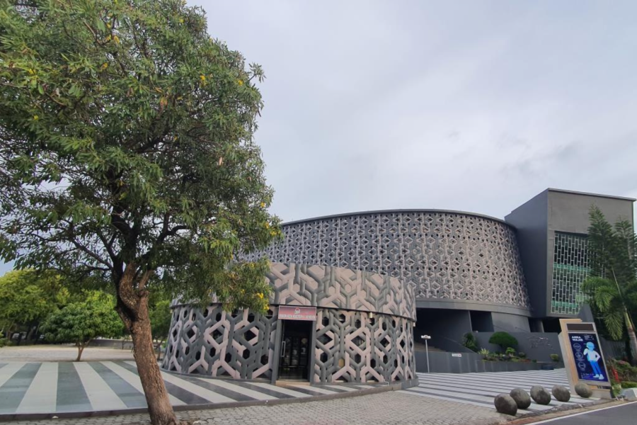 The front part of the Aceh Tsunami Museum building has round designs and a tall green tree next to the building.