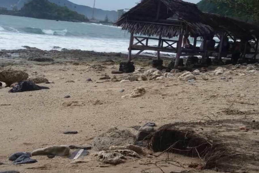 Stones and dead leaves cover the beautiful beach sands. In the background are some gazebos built on the shore of Aceh beach.