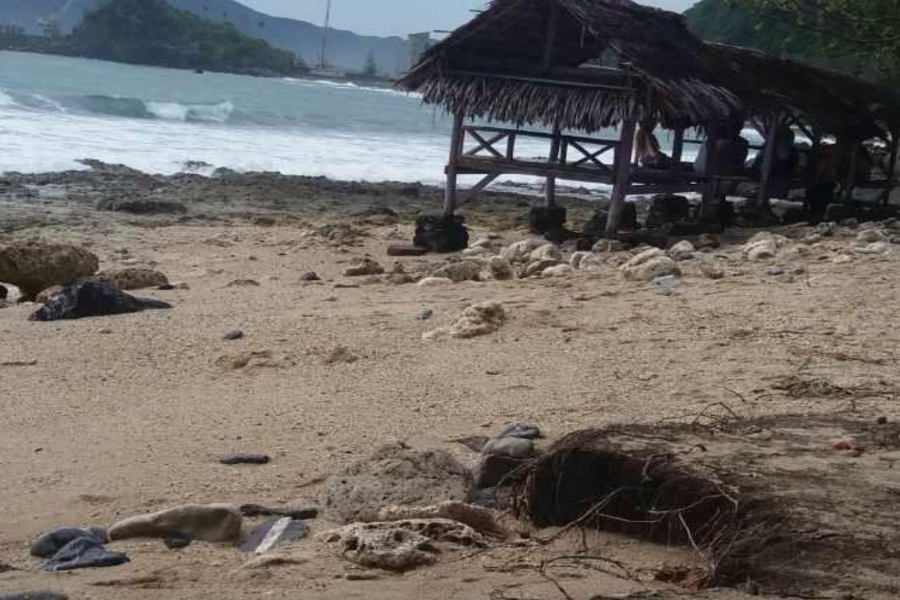 Stones and dead leaves cover the beautiful beach sands. In the background are some gazebos built on the shore of Aceh beach. 