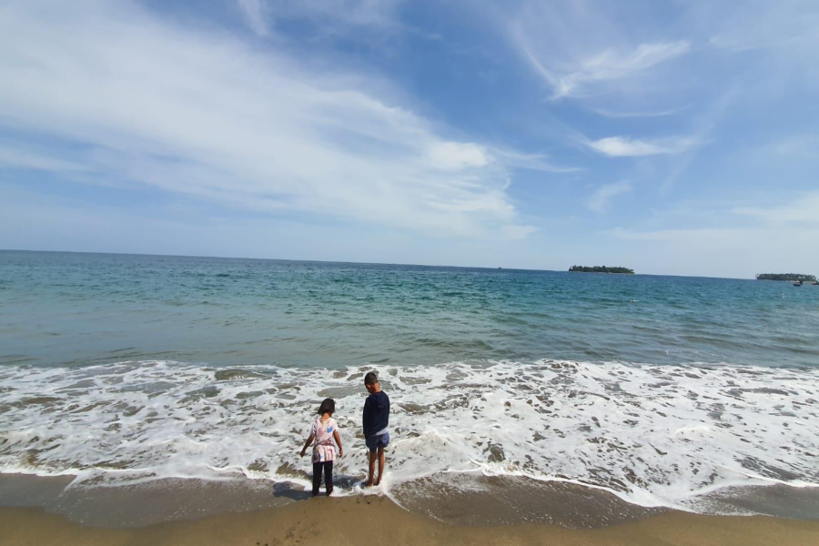 One boy and girl stand on the beach in Aceh and play with the calm wave. In the background is the beautiful bright blue sky.