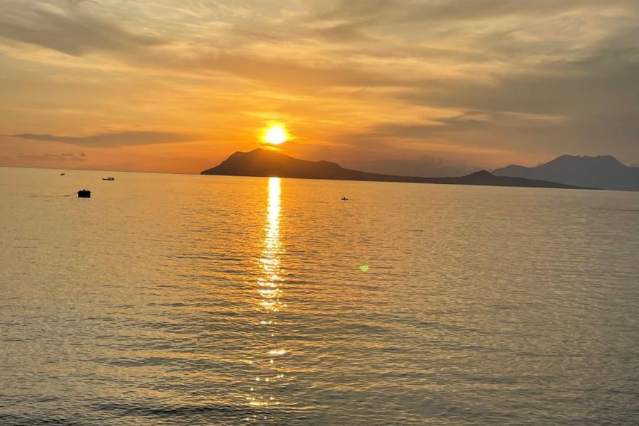 Pemandangan indah laut Celebes saat matahari terbenam. Langit berubah warna menjadi oranye dan refleksi matahari dapat terlihat jelas di air laut yang tenang.