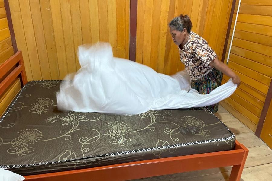 A lady putting a white sheet on the bed. 