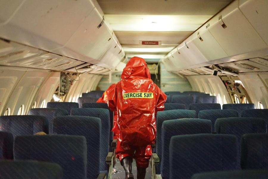 A person wearing orange hazmat suit walking inside of a plane