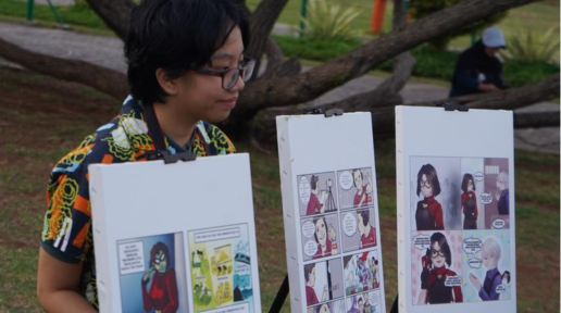 One of the winners of comic competition poses with her winning comic strip in front of Monas